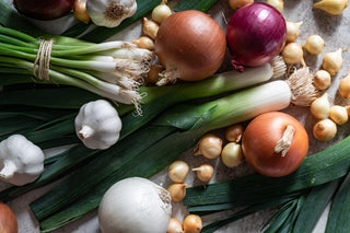A mixture of bunched green onions, red onions, white onions, yellow onions and garlic