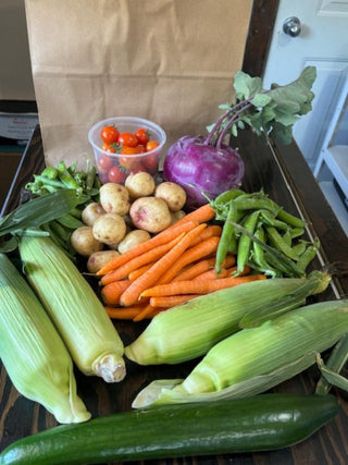 Assorted garden fresh vegetables, including corn, carrots, baby potatoes, peas and kohlrabi. The cherry tomatoes and cucumber are grown in our greenhouses at Maple Park Farm.
