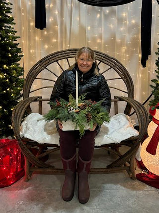 Person holding a festive centerpiece in a decorated room with Christmas trees and lights.