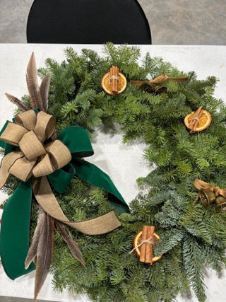 Christmas wreath with fresh greenery, a large double bow, orange slices, cinnamon and bells.  Feathers also accent the bow.