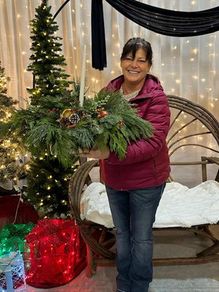 Person holding her centerpiece in a decorated room with lights and a tree.