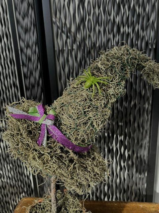 A handcrafted moss witch hat. Each hat has a whimsical, curved shape and is accented with natural touches like twine, a dried flower, and a small succulent, feathers and grasses creating a rustic and magical display.