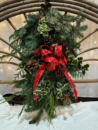 Decorative wreath with fresh evergreens,  red ribbon, fresh holly and pinecones.