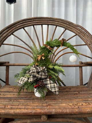 Decorative whimsical tree made with fresh greenery, plaid ribbon, pinecones, bells and cinnamon sticks on a wooden bench.