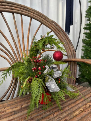Decorative Christmas arrangement with greenery, red ornaments, fresh rose hips and silver ribbons on a wooden chair.
